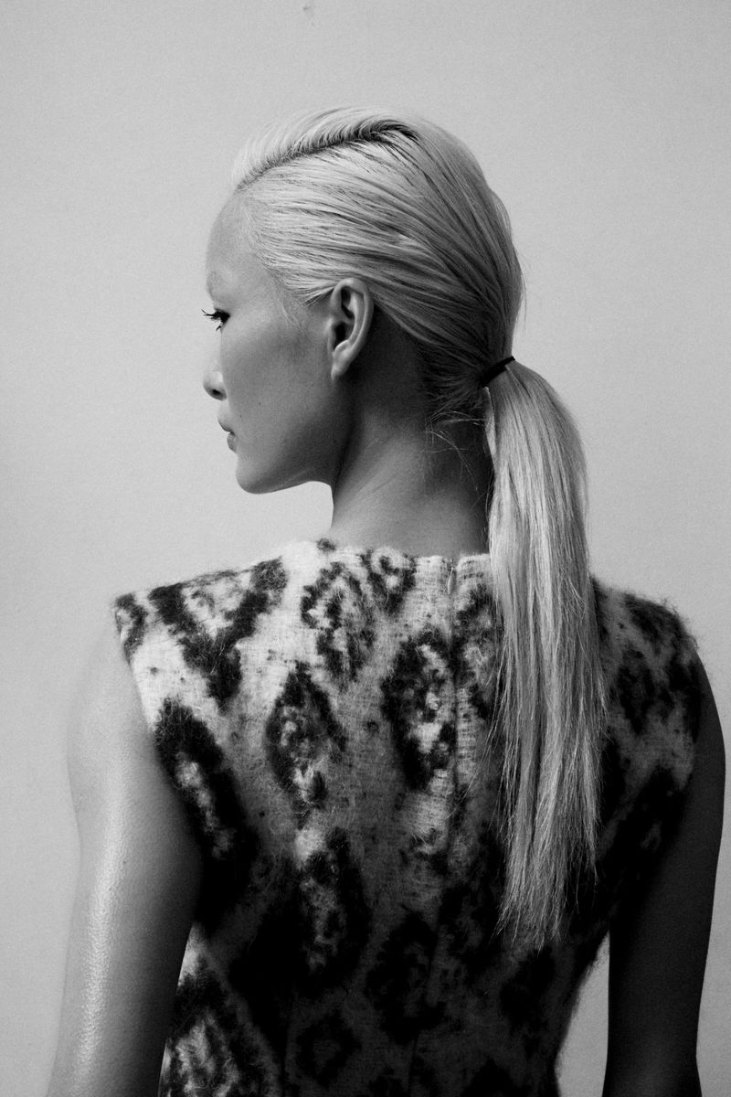 Model with blonde hair tied in a ponytail wearing a patterned sleeveless top against a plain light background