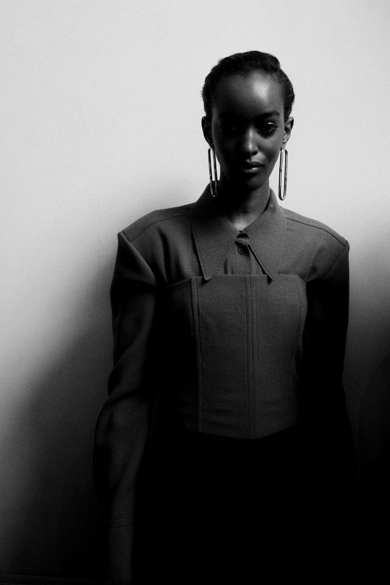 Portrait of a Black woman in a collared, structured top and hoop earrings against a light background in a studio setting with soft lighting.