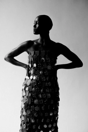 Model wearing a strapless medallion-adorned dress posing against a plain grey seamless background in monochrome.