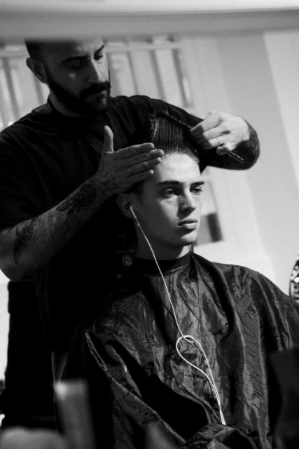 Black and white portrait of a barber cutting a young man's hair, both indoors, with a focus on hair and hairstyling.