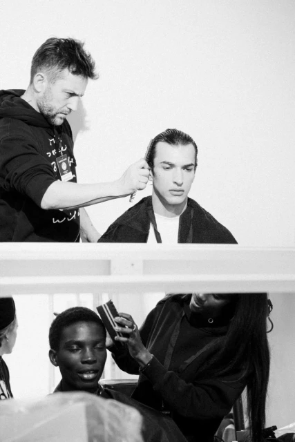 Black and white shot of three people in a backstage setting, two people styling hair and one person sitting at a vanity.