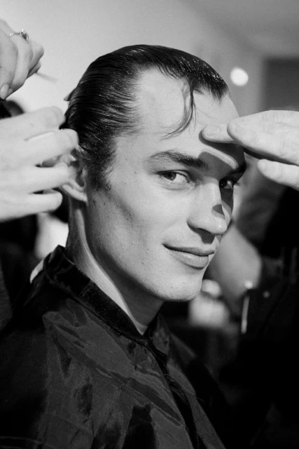 Black and white studio shot of a handsome male getting a haircut, fingers adjusting his hair for the stylist to trim.