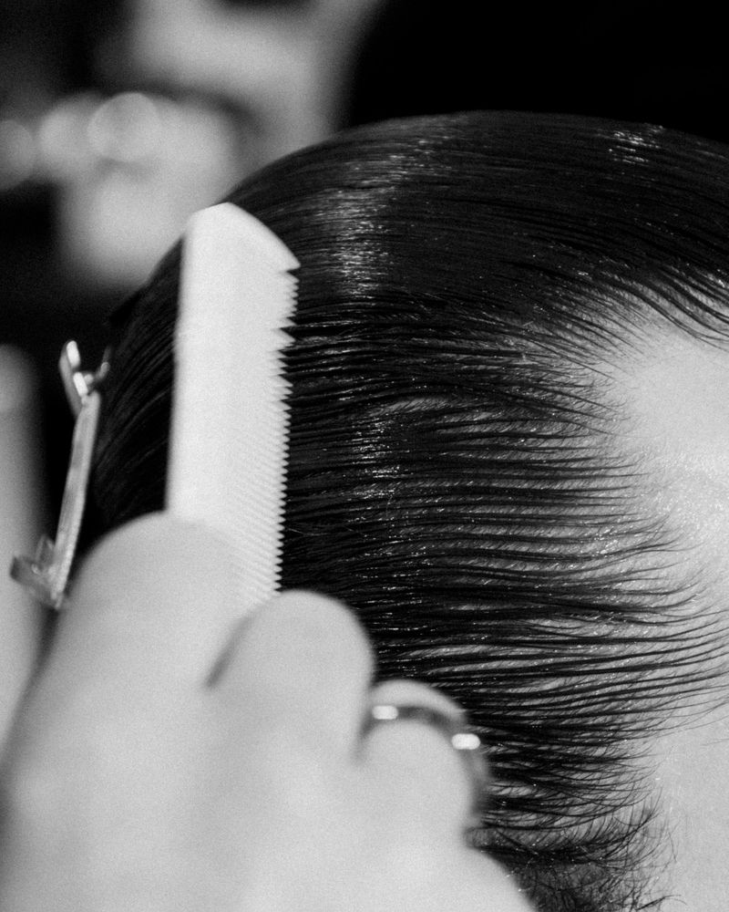 Close-up shot of a person's black hair being styled with a white comb and secured with a metal hair clip, focusing on grooming details.