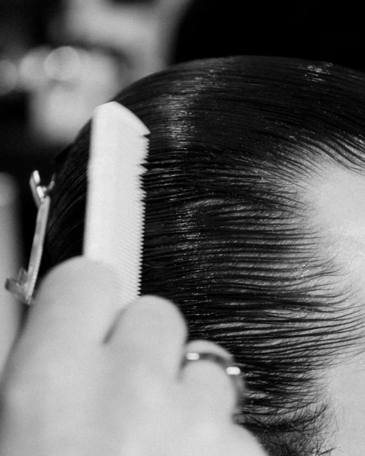 Close-up shot of a person's black hair being styled with a white comb and secured with a metal hair clip, focusing on grooming details.