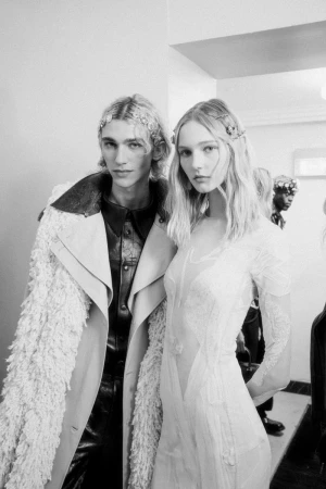 Two models standing backstage wearing designer outfits, captured in a monochrome documentary photograph by Vincent Fandos.