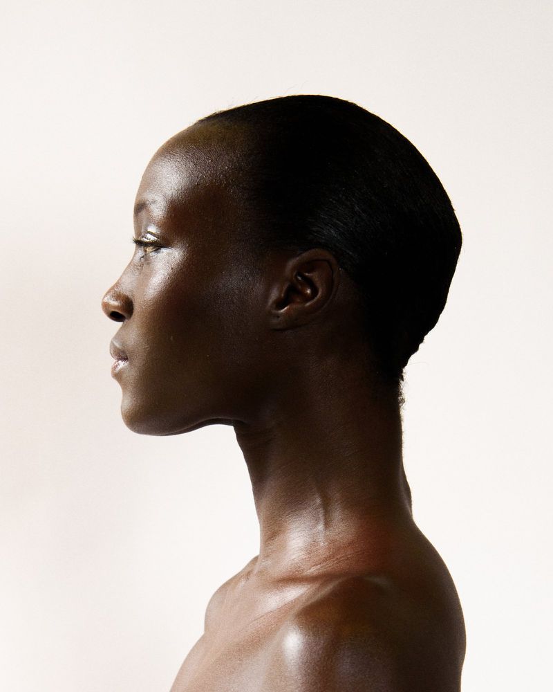 Profile shot of an adult Black woman with slicked-back hair against a light background, showcasing smooth skin and neck. Minimalist studio portrait.