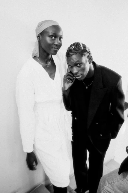 Black and white portrait of two adults standing in formal wear: a woman in a dress and headscarf and a man in a suit.