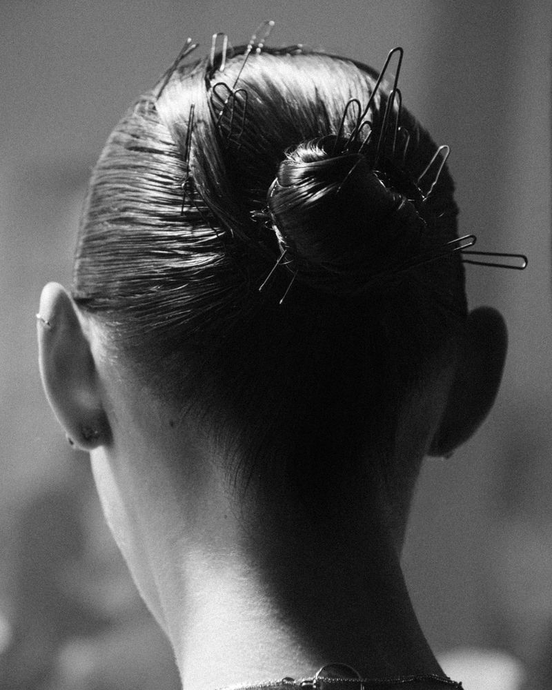 Black and white portrait from behind of a woman's head with dark hair styled in a bun and held in place with numerous bobby pins.