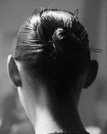 Black and white portrait from behind of a woman's head with dark hair styled in a bun and held in place with numerous bobby pins.