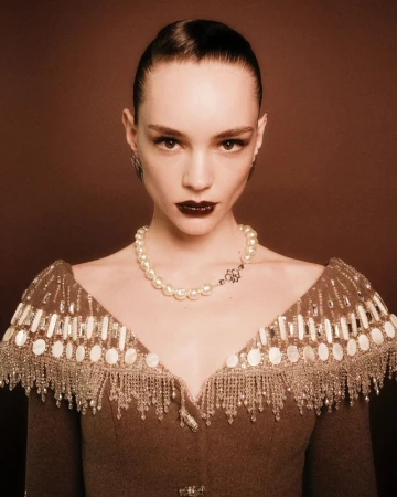 Portrait of a female fashion model with dark lipstick and elegant, beaded pearl-embellished couture against a muted brown backdrop.