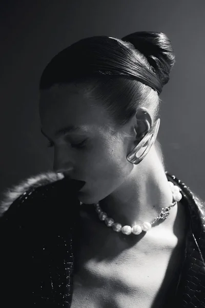 Model with sleek updo wearing a large pearl necklace and statement ear cuff in dramatic black and white lighting