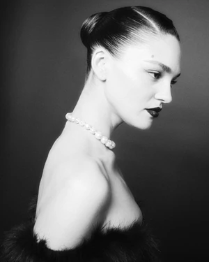 Model with slicked-back bun wearing a pearl choker and dark lipstick against a dark background