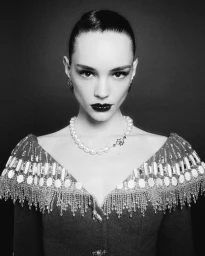 Model wearing a pearl necklace and embellished V-neck garment in a black and white portrait by Vincent Fandos for Georges Hobeika.