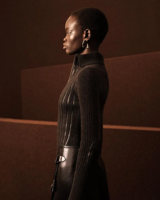 Profile shot of a dark-skinned woman with short hair wearing a ribbed, dark top and silver earrings against a brown background.