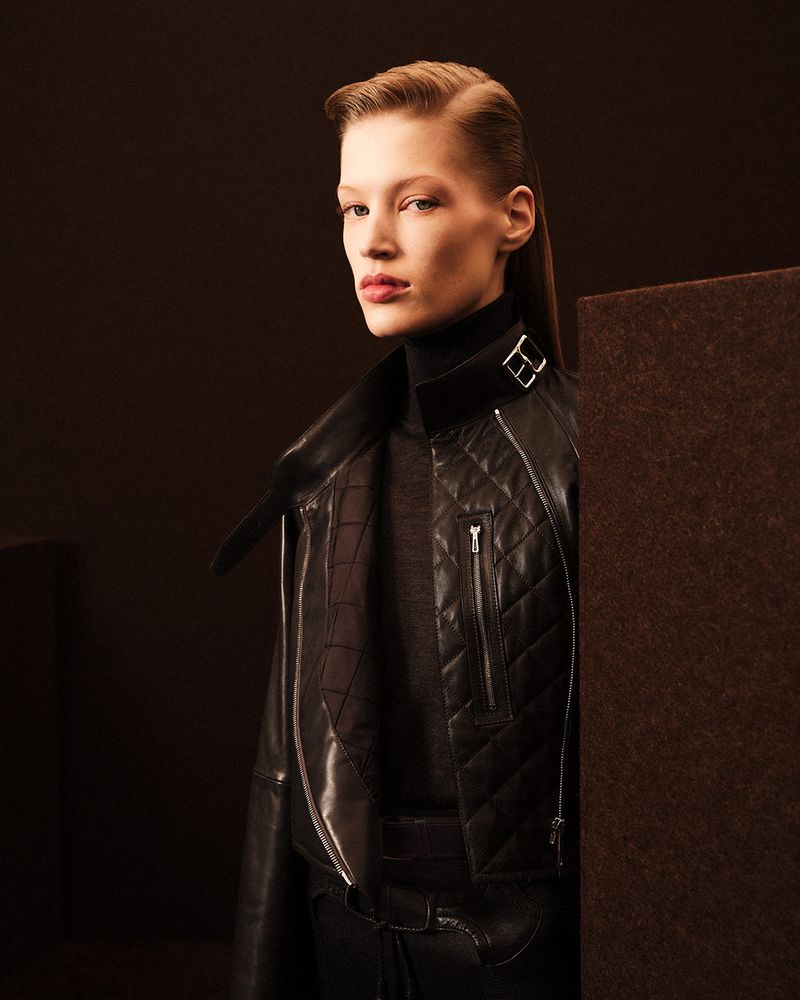 Model wearing a black leather quilted jacket and turtleneck against a dark neutral studio background
