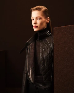 Model wearing a black leather quilted jacket and turtleneck against a dark neutral studio background