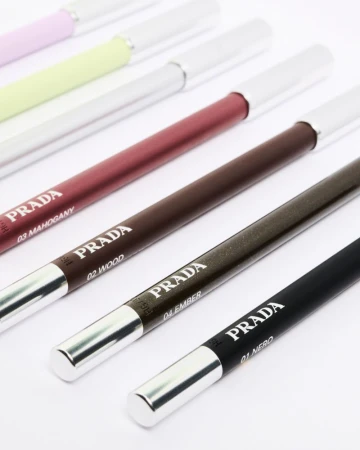 Close-up of Prada eyeliner pencils in assorted shades including mahogany, wood, ember, and nero arranged diagonally on a white surface.