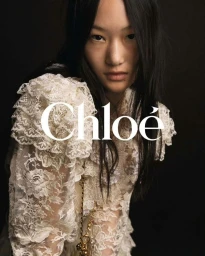 Model wearing a white lace dress with ruffles against a dark background for Chloé