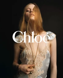 Model in white satin lace slip dress with gold necklaces against dark background for ChloÃ©