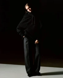 Model Lulu Tenney wearing a black knitted sweater and dark trousers under dramatic low-key lighting for Hermes