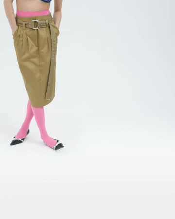 Model wearing a khaki belted midi skirt, vibrant pink tights, and black pointed kitten heels against a white studio backdrop.