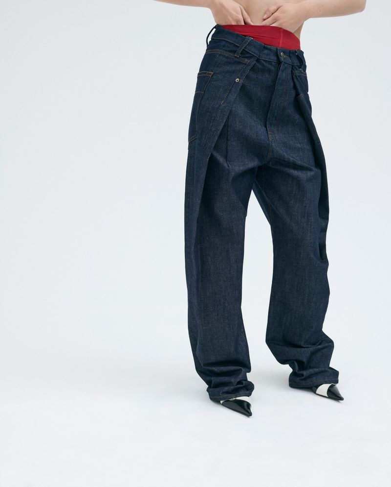 A fashion-forward image featuring a person wearing baggy, dark-wash denim jeans and black and white heels against a stark white backdrop.