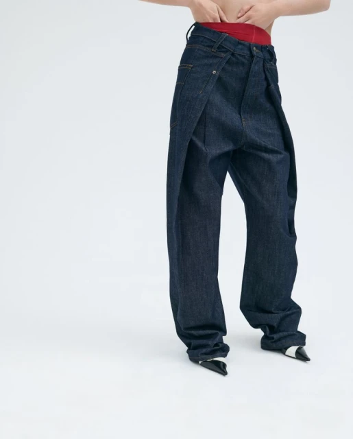 A fashion-forward image featuring a person wearing baggy, dark-wash denim jeans and black and white heels against a stark white backdrop.