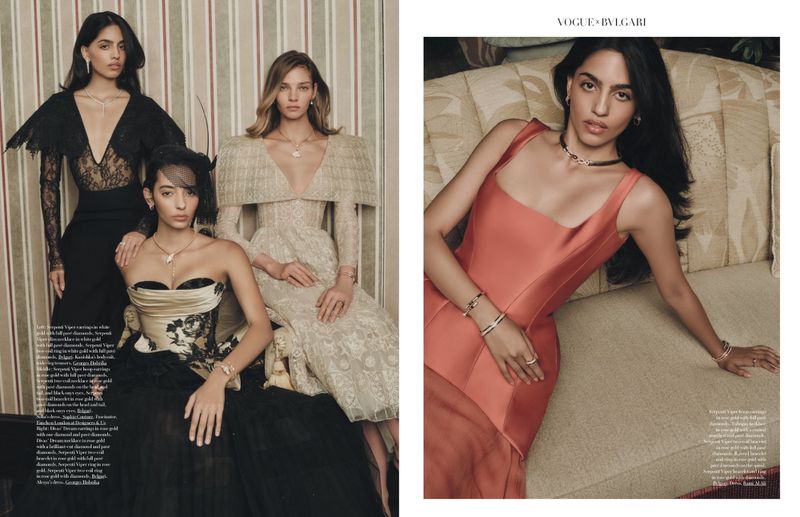 Three women in elegant gowns and jewelry pose against a striped wall. A fourth woman in a coral dress reclines on a patterned couch.