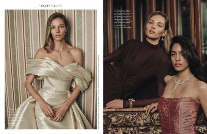 Two women pose in luxury dresses and jewelry for a fashion editorial, showcasing Bulgari and Vogue collaboration, indoors with muted tones.