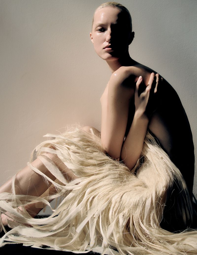 Striking studio portrait of a fair-skinned woman with blonde hair styled as a gown, illuminated by dramatic side lighting.