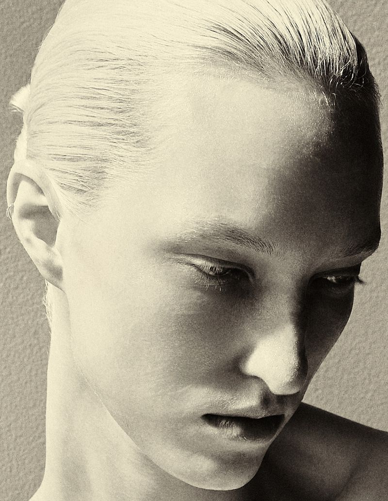 Monochrome portrait of an adult woman with blonde hair, looking down pensively, with soft lighting and a neutral studio backdrop.