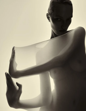 Conceptual studio portrait of a nude adult female with hands on a semi-transparent veil, shot with diffused lighting against an off-white background.
