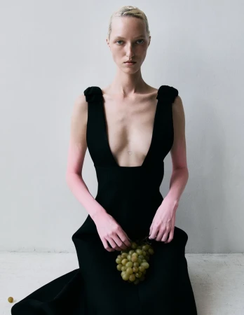 Woman in black dress holds grapes against a white background, fashion editorial, studio lighting, high fashion, elegant style.