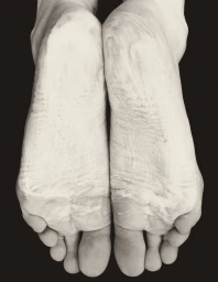 Close-up of the soles of two feet coated in textured white cream against a solid black background.