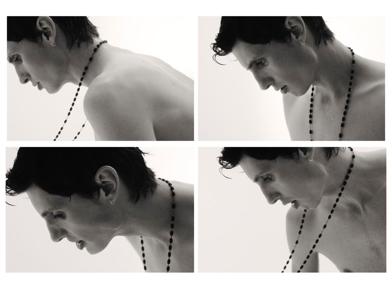 A monochrome collage of a shirtless person with short dark hair looking down while wearing a rosary necklace in a bright studio.