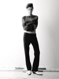 Model Jack Stewart posing in a cropped knit sweater, black trousers, and white pointed boots against a white studio wall for Rain Magazine.