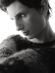 Black and white close-up portrait of a man in a textured knit sweater looking down against a bright white background.