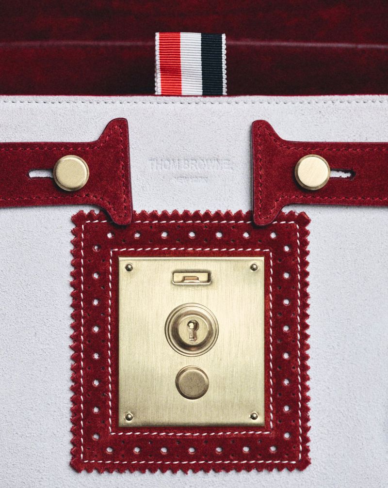 Close-up of a white leather Thom Browne handbag with a gold lock and a red suede trim, featuring the brand's signature grosgrain ribbon.