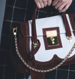 Close-up of a white and burgundy leather handbag with gold hardware held against a plaid skirt