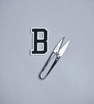 Letter B chenille patch and metal thread snips on grey textured backdrop