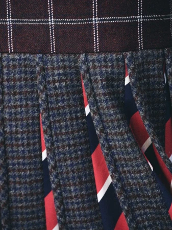 Detailed close-up view of pleated plaid skirt featuring houndstooth pattern and vibrant multi-colored stripes for Thom Browne