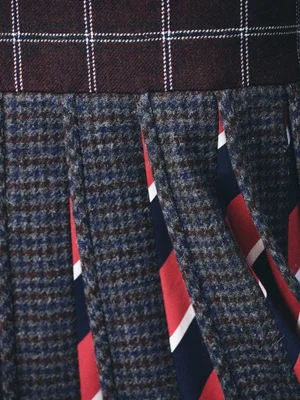 Detailed close-up view of pleated plaid skirt featuring houndstooth pattern and vibrant multi-colored stripes for Thom Browne