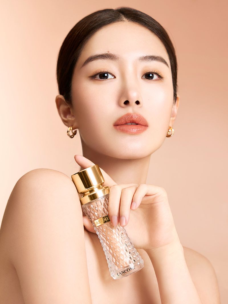Close-up shot of an Asian woman holding a Lancome perfume bottle. Beauty and skincare product promotion on beige background.