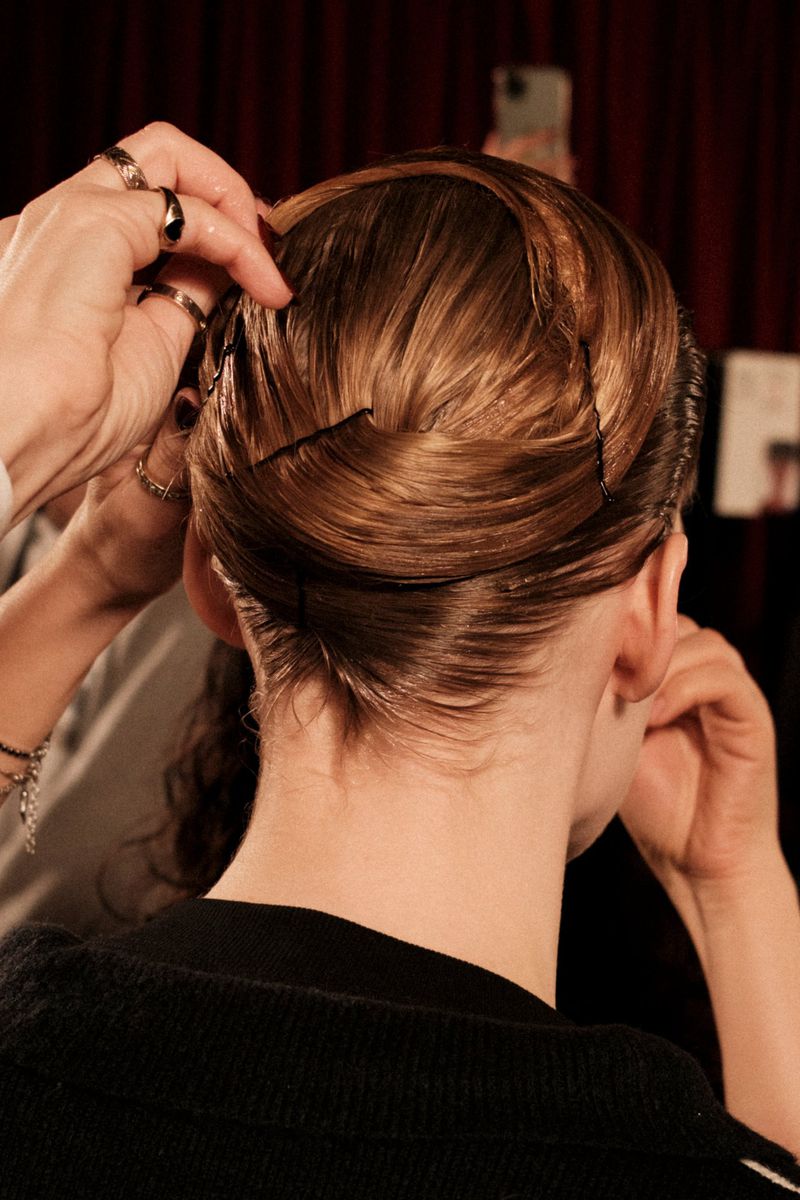 Close-up shot of a hairstylist pinning up auburn hair; styled updo hairstyle with hair pins and a partial view of a black sweater.