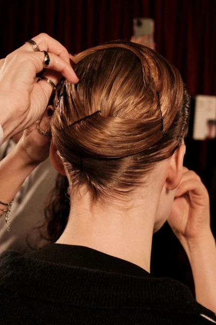 Close-up shot of a hairstylist pinning up auburn hair; styled updo hairstyle with hair pins and a partial view of a black sweater.