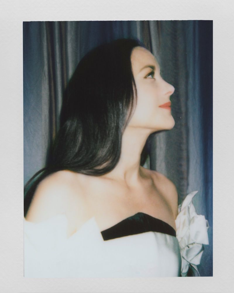 Profile view of a fair-skinned woman with long dark hair, wearing a strapless dress with black and white accents, looking upward.