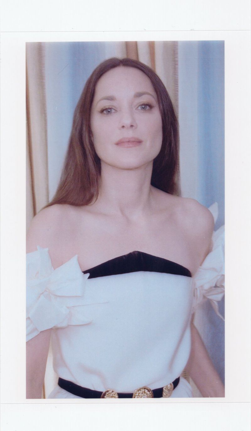 Elegant portrait of an adult woman with long brown hair, wearing a white dress with black trim against a patterned backdrop.