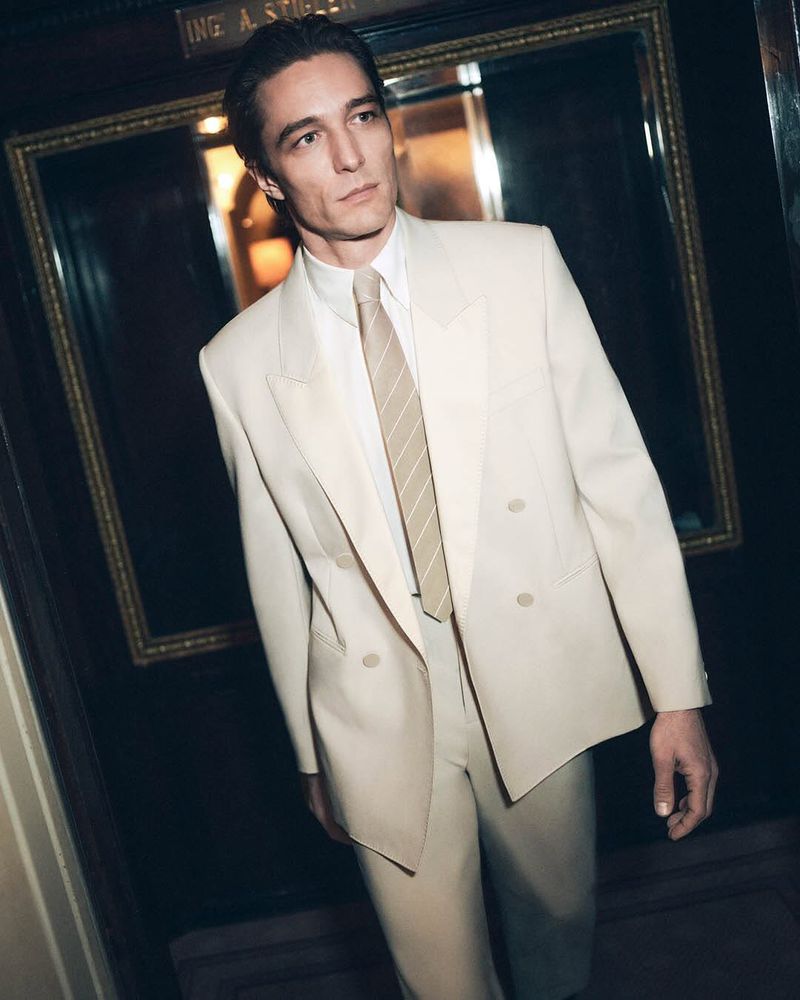 Man wearing a cream double-breasted suit with a white shirt and striped tie standing indoors