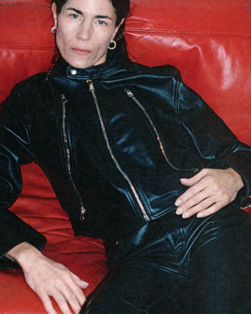 Woman in black leather jacket sits on red couch. Fashion-style portrait. Casual, youthful and modern design.
