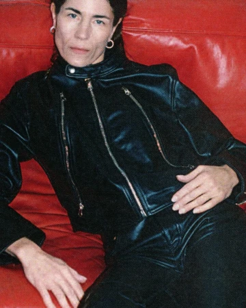 Model wearing a black leather jacket seated against a bright red cushioned background for MM6 Maison Margiela